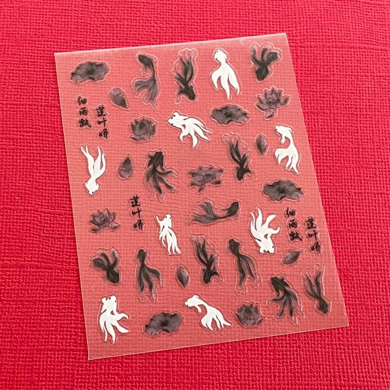 May include: Clear sticker sheet with a repeating pattern of black and white koi fish, lily pads, and Chinese characters. The sticker sheet is on a red background.