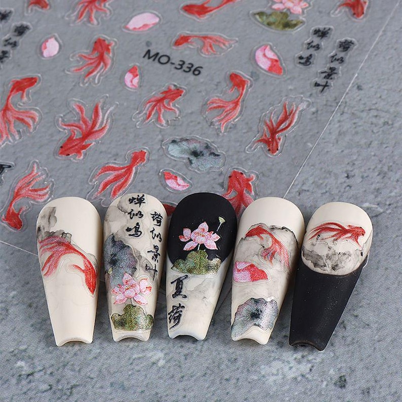 May include: Nail art stickers featuring red koi fish and floral designs. The stickers are on a clear sheet with the text "MO-336". Five painted nails showcase similar designs, including koi fish, lotus flowers, and Chinese calligraphy.