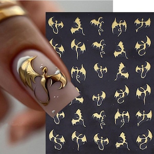 May include: Gold dragon nail art stickers on a black background. The stickers feature a detailed dragon design with outstretched wings. One nail is painted with a gold dragon design. The nail art stickers are a metallic gold color.