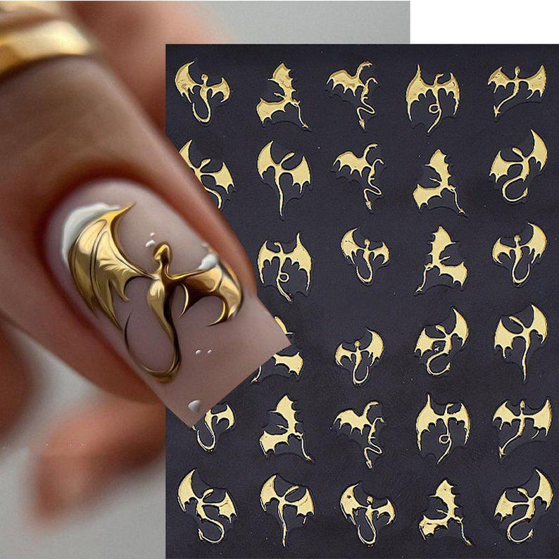 May include: Gold dragon nail art stickers on a black background. The stickers feature a detailed dragon design with outstretched wings. One nail is painted with a gold dragon design. The nail art stickers are a metallic gold color.