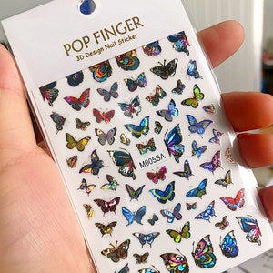 May include: A sheet of nail stickers with a variety of colorful butterfly designs. The stickers are iridescent and have a 3D effect. The sheet is labeled "POP FINGER 3D Design Nail Sticker" and "M005SA".