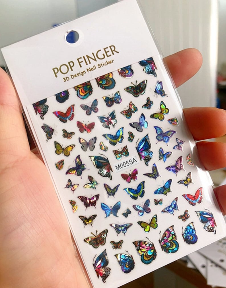May include: A sheet of nail stickers with a variety of colorful butterfly designs. The stickers are iridescent and have a 3D effect. The sheet is labeled "POP FINGER 3D Design Nail Sticker" and "M005SA".