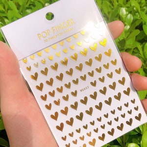 Op de afbeelding: Gouden hart nagelstickers op een wit vel met de tekst "POP FINGER 3D Design Nail Sticker" en "WG622".