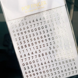May include: A sheet of silver nail stickers with numbers 0 through 9. The sheet is labeled "POP FINGER 3D Design Nail Stickers" and "Me099".