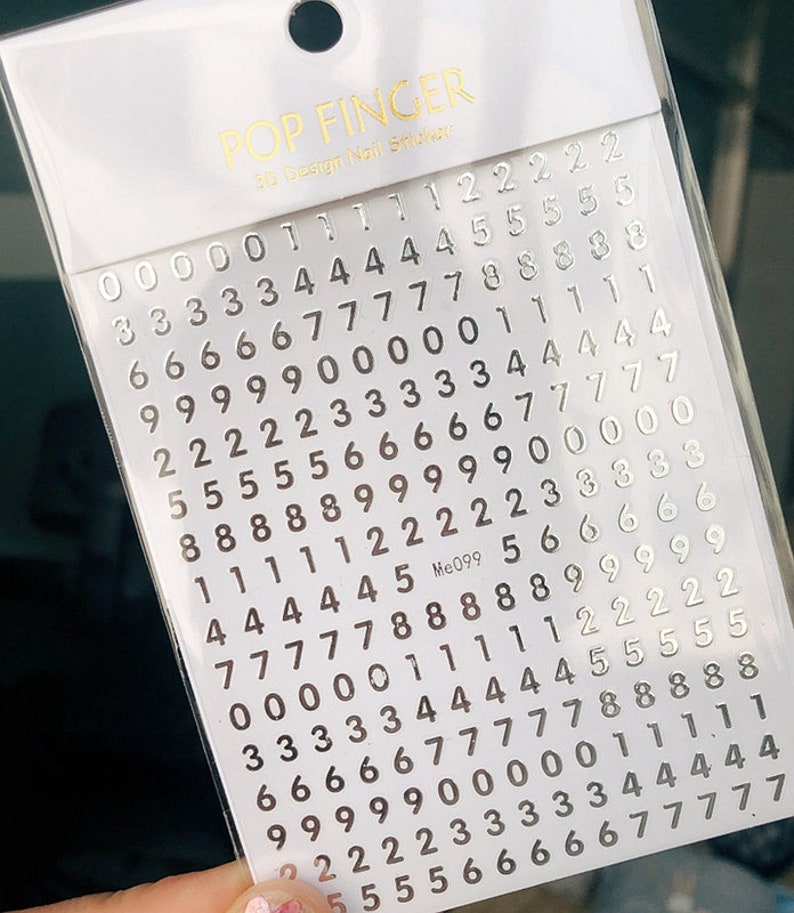 May include: A sheet of silver nail stickers with numbers 0 through 9. The sheet is labeled "POP FINGER 3D Design Nail Stickers" and "Me099".