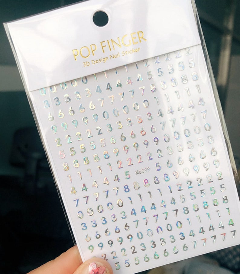 May include: A sheet of iridescent holographic nail stickers with numbers 0-9. The stickers are on a white background with the text "POP FINGER 3D Design Nail Sticker" and "Me099" printed in gold.