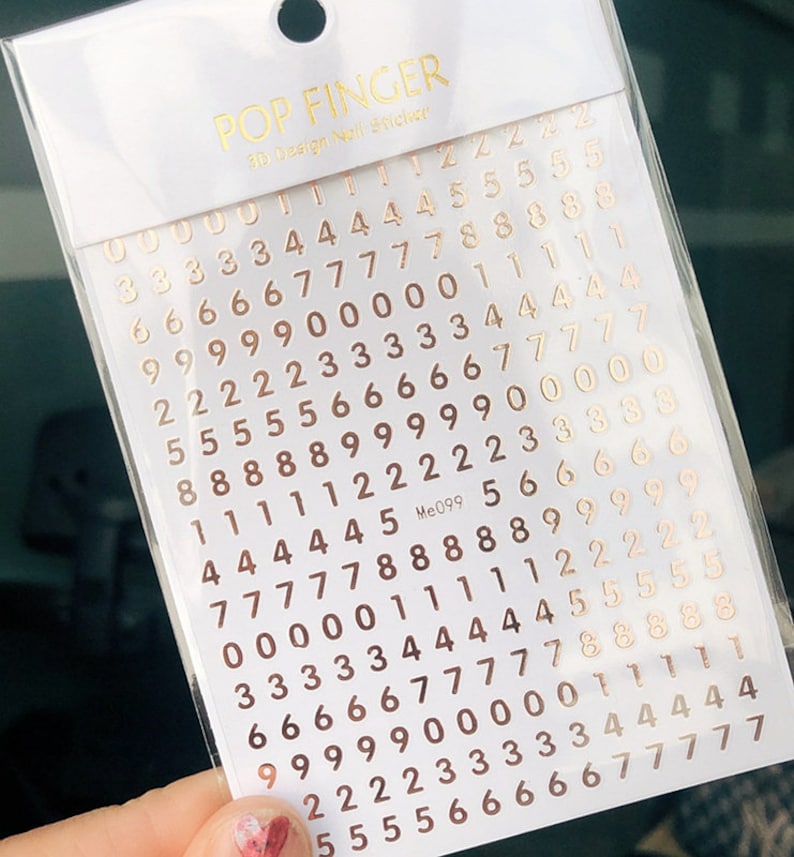 May include: A sheet of gold-colored number stickers for nail art. The numbers 0 through 9 are arranged in rows on a white background. The sheet is labeled "POP FINGER 3D Design Nail Sticker" and "Me099".