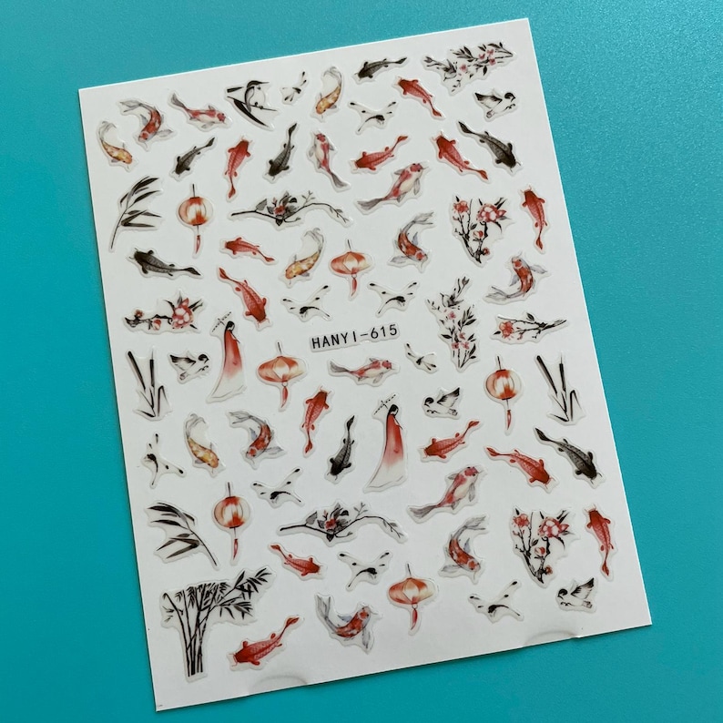 May include: A sheet of nail art stickers featuring an Asian-inspired design. The stickers include koi fish, floral elements, and figures in red, black, and white. The text "HANY I-615" is printed on the sheet.