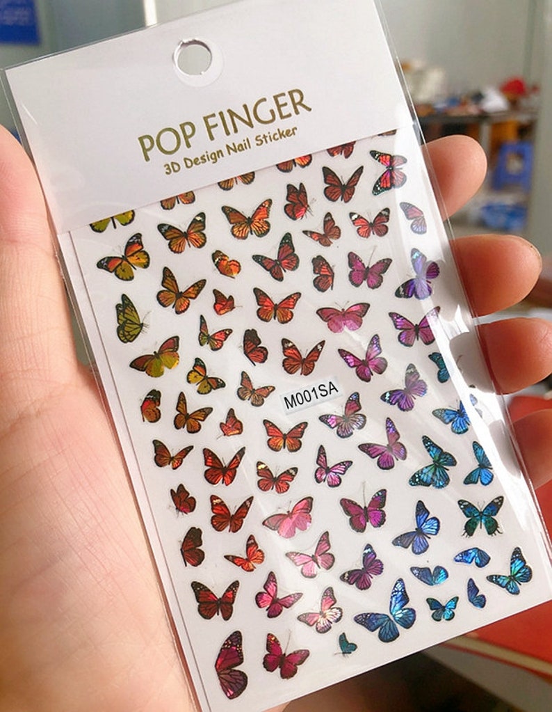 May include: A sheet of 3D nail stickers featuring colorful butterfly designs. The stickers are arranged in rows and columns on a white background. The text "POP FINGER 3D Design Nail Sticker" is printed at the top of the sheet. The code "M001SA" is printed in the center of the sheet.