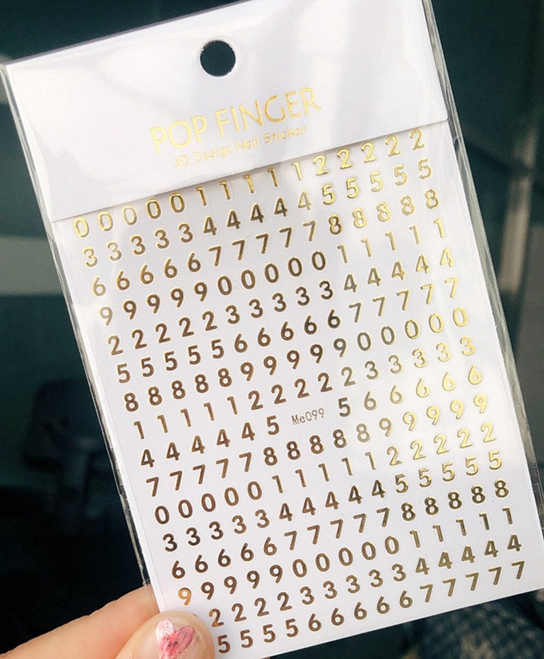 May include: A sheet of gold number stickers with the text "POP FINGER 3D Design Nail Sticker" and "Me099" printed on the sheet.
