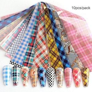 Puede incluir: Diez hojas de lámina de transferencia para uñas con estampado de cuadros de colores. La lámina es translúcida y tiene una variedad de colores y patrones, incluyendo azul, rojo, amarillo y rosa. La lámina está empaquetada en una bolsa de plástico transparente con el texto "10pcs/pack" impreso en ella.