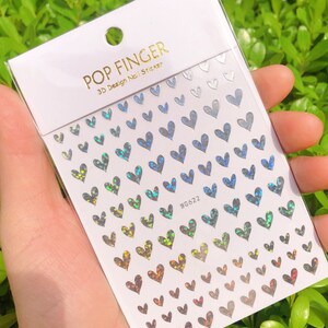 Op de afbeelding: Een vel met regenboogkleurige, hartvormige nagelstickers. De stickers zijn in rijen gerangschikt en tonen een kleurverloop van blauw naar groen naar rood. Het vel is gelabeld met "POP FINGER 3D Design Nail Sticker" en "WG622".