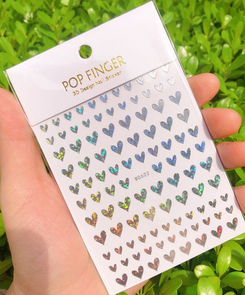 Op de afbeelding: Een vel met regenboogkleurige, hartvormige nagelstickers. De stickers zijn in rijen gerangschikt en tonen een kleurverloop van blauw naar groen naar rood. Het vel is gelabeld met "POP FINGER 3D Design Nail Sticker" en "WG622".