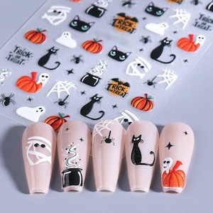 May include: Halloween-themed nail art stickers featuring pumpkins, black cats, ghosts, spiders, and cobwebs. The stickers are on a clear sheet, with nail designs including a mummy, cauldron, spiderweb, black cat, and pumpkin with a skull.