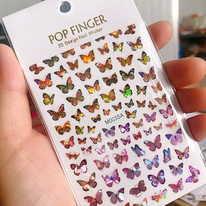 May include: A sheet of iridescent butterfly nail stickers. The stickers are in various shades of pink, purple, orange, and yellow. The sheet is labeled "POP FINGER 3D Design Nail Sticker" and "M003SA".