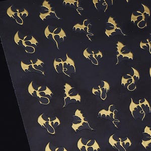 May include: Black sheet with a repeating pattern of gold-colored dragon silhouettes. The dragons have outstretched wings and detailed bodies, creating a textured effect. The design is evenly spaced across the surface.