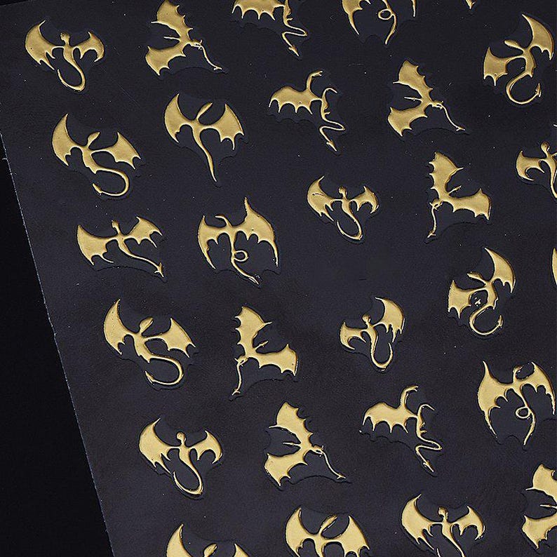 May include: Black sheet with a repeating pattern of gold-colored dragon silhouettes. The dragons have outstretched wings and detailed bodies, creating a textured effect. The design is evenly spaced across the surface.