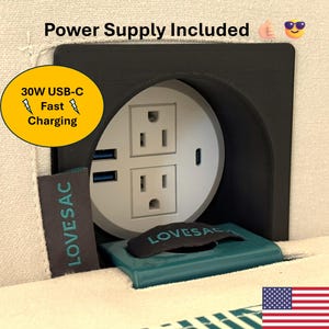 May include: A black circular power hub integrated into light-colored fabric, featuring two standard electrical outlets, two USB-A ports, and one USB-C port. Text reads Power Supply Included and 30W USB-C Fast Charging. A teal tag displays LOVESAC.