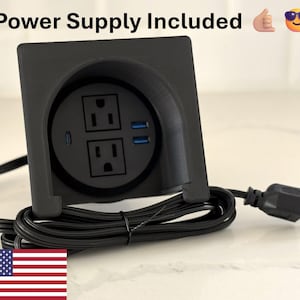 May include: Black power outlet with two standard outlets and two USB ports. The outlet is mounted on a black surface and has a black power cord.