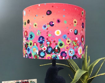 May include: A pink lampshade with a colorful abstract pattern of circles and dots. The lampshade is on a black lamp base shaped like a crow.