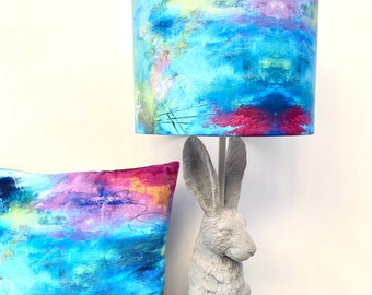 May include: A lampshade with a blue, pink, and yellow abstract design sits on top of a gray rabbit-shaped lamp base.