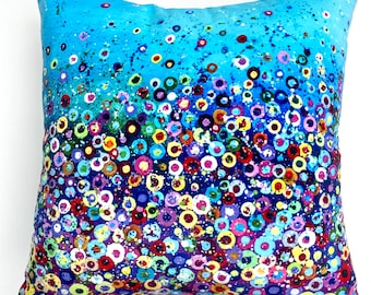 May include: A blue cushion with a colourful abstract pattern of circles and dots. The cushion is made of soft fabric and has a zip closure.