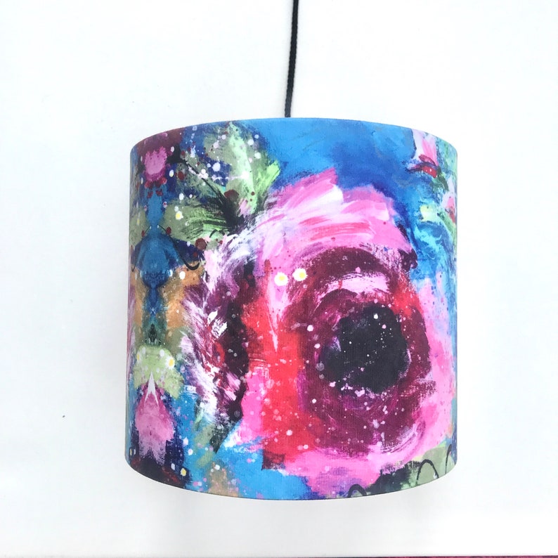 May include: A colourful floral lampshade featuring a large pink and red flower in the centre. The background is a mix of blue, green and white.