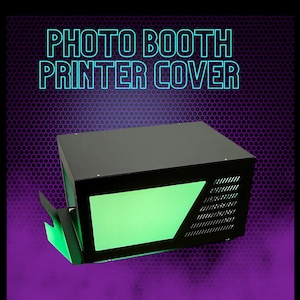 May include: Black photo booth printer cover with a green light panel and a black grill on the side. "PHOTO BOOTH PRINTER COVER" is written in white text on a blue background.