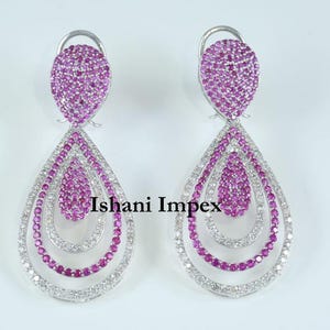 May include: A pair of silver dangle earrings featuring pink gemstones and white diamonds. The earrings are teardrop shaped with three layers of stones.