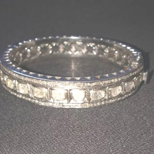 Puede incluir: Un brazalete de plata con una fila de pequeños diamantes cuadrados engastados en una banda decorativa.