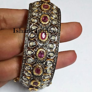 Puede incluir: Un brazalete de plata y oro con una fila de piedras preciosas rosas y una fila de pequeños diamantes. El brazalete está decorado con un diseño floral.