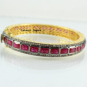 Può includere: Bracciale rigido in oro con una fila di pietre quadrate rosa e un bordo di piccole pietre bianche. Il bracciale è inciso con il testo "Ishani Impex".
