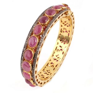 May include: A gold bangle bracelet featuring a delicate filigree design. The bracelet is embellished with a row of pink gemstones and small diamonds.