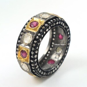 May include: A band ring featuring alternating square gold settings with round red rubies and silver-toned settings with white stones. The edges are lined with small black beads and the text Ishani Impex is visible on the inner band surface.