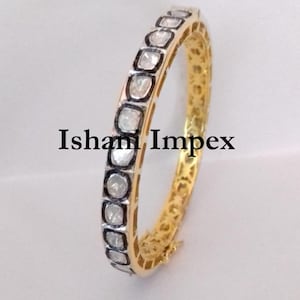 Puede incluir: Un brazalete de oro con una fila de pequeños diamantes cuadrados engastados en plata. El brazalete está abierto y tiene un cierre de bisagra.