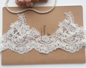 May include: Ivory lace trim with a delicate floral pattern. The lace has a scalloped edge and is perfect for adding a touch of elegance to any project.