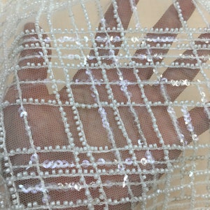 May include: White beaded and sequined fabric with a grid pattern. The fabric is sheer and has a delicate, elegant look.