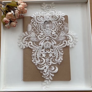 Op de afbeelding: Witte kant applique met een bloemenmotief. De kant is delicaat en ingewikkeld, met een verscheidenheid aan bloemenmotieven. De applique is perfect om een ​​toets van elegantie aan elk project toe te voegen.