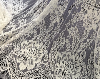 May include: Close-up of white floral lace fabric. The lace features a delicate pattern of flowers and leaves, with intricate details and a soft texture. The fabric is semi-sheer, with a subtle sheen, and is suitable for various craft projects.
