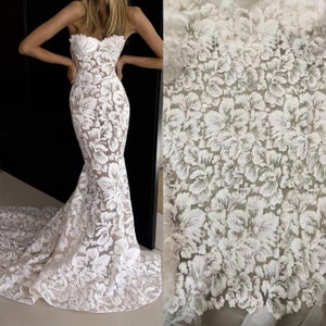 May include: White floral lace fabric with a delicate, raised pattern. The fabric is shown on a dress and as a separate swatch.