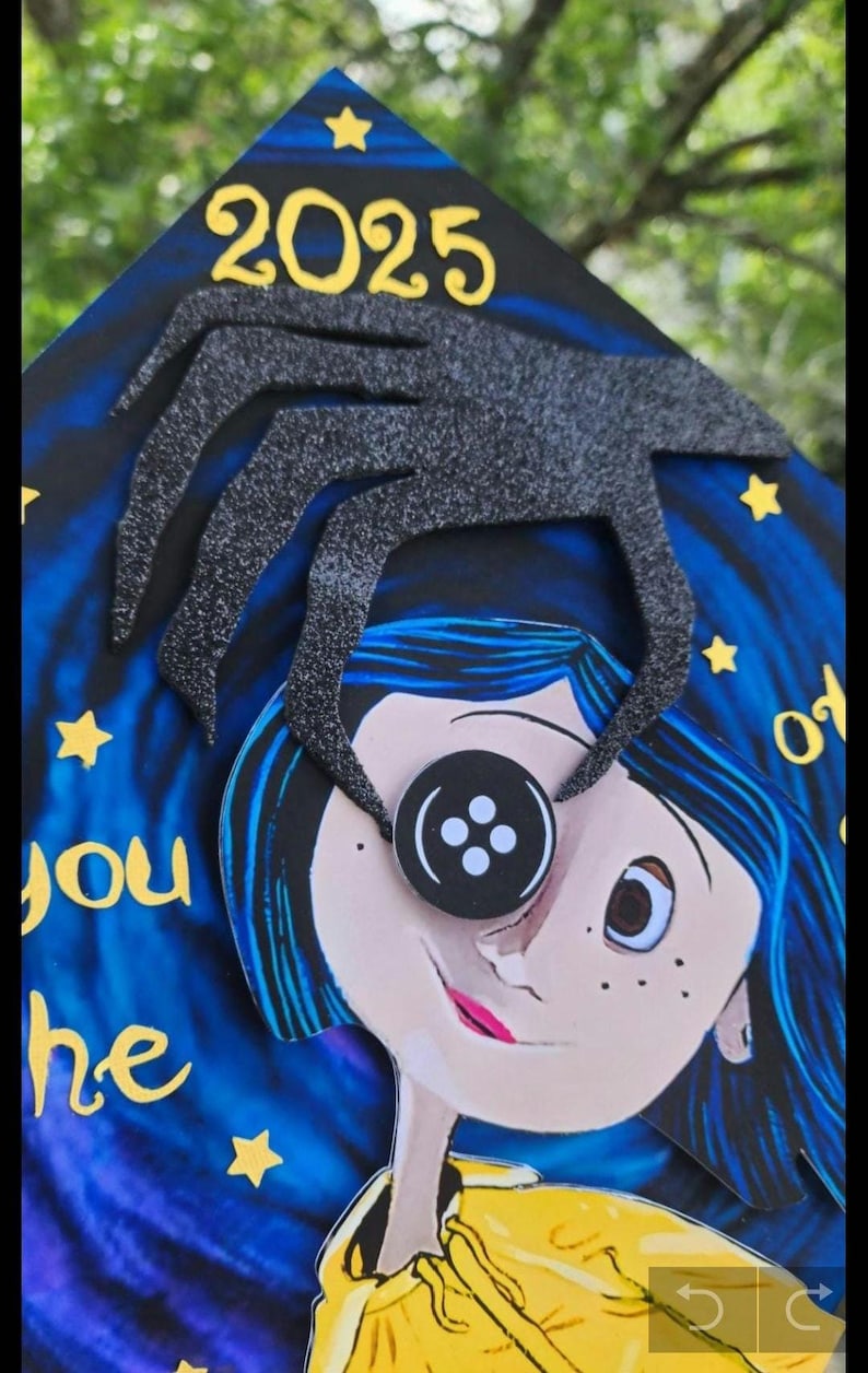 May include: A graduation cap featuring a cartoon illustration of a character with blue hair and a button eye. The cap has the year 2025 and a black spider-like design. The background is a starry night sky with text.