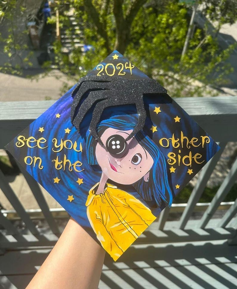 May include: A decorated graduation cap featuring a character with a button eye, blue hair, and a yellow jacket. The cap has the text "See you on the other side" and "2024" with star accents. A black spider-like embellishment is on top.