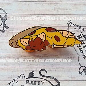 Peut inclure: Une épingle en émail dorée représentant deux rats de dessin animé endormis sur une part de pizza. La pizza est jaune avec des pepperoni rouges et une croûte brune. L'épingle porte le texte "Ratty Creations" sur le côté.