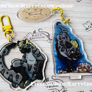 May include: Two acrylic keychains featuring cartoon hyenas. One keychain is blue with a hyena in a blue and gray patterned design. The other keychain is clear with a hyena in a gray and black patterned design. Both keychains have the text "Ratty Creations" printed on them.