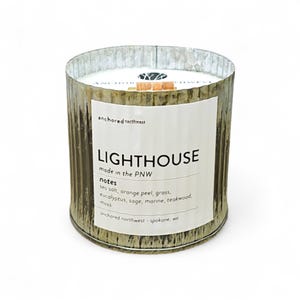 May include: A cylindrical candle in a distressed metal container. The label reads "LIGHTHOUSE" with scent notes listed below. The candle is from "anchored northwest" and made in the PNW.