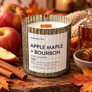 May include: A cylindrical candle in a corrugated metal container with a white label reading APPLE MAPLE + BOURBON, made in the PNW, and listing notes of apple, cinnamon, orange, bourbon, butter, coconut, maple, and vanilla with a wood wick.