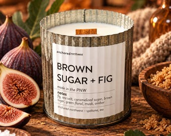 May include: A cylindrical candle in a corrugated metal container with a white label reading Brown Sugar + Fig, made in the PNW, with notes of fig, sea salt, caramelized sugar, brown sugar, green floral, musk, and amber, featuring a wooden wick.