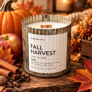 May include: A cylindrical candle in a corrugated metal container with a white label reading FALL HARVEST, anchored northwest, made in the PNW, and notes of crisp apple, warm pumpkin, cinnamon, clove, nutmeg, vanilla, and cedar with a wood wick.