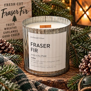 May include: A cylindrical candle in a corrugated galvanized metal container with a white label reading Anchored Northwest Fraser Fir, made in the PNW, with notes of lemon peel, cypress, evergreen, cedar, fir, amber, and moss, and a wooden wick.