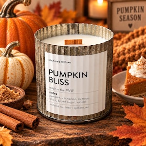 May include: A scented candle in a corrugated metal container with a white label reading PUMPKIN BLISS, anchored northwest, made in the PNW, and notes of pumpkin, cinnamon, nutmeg, clove, brown sugar, and vanilla. The candle has a wooden wick.
